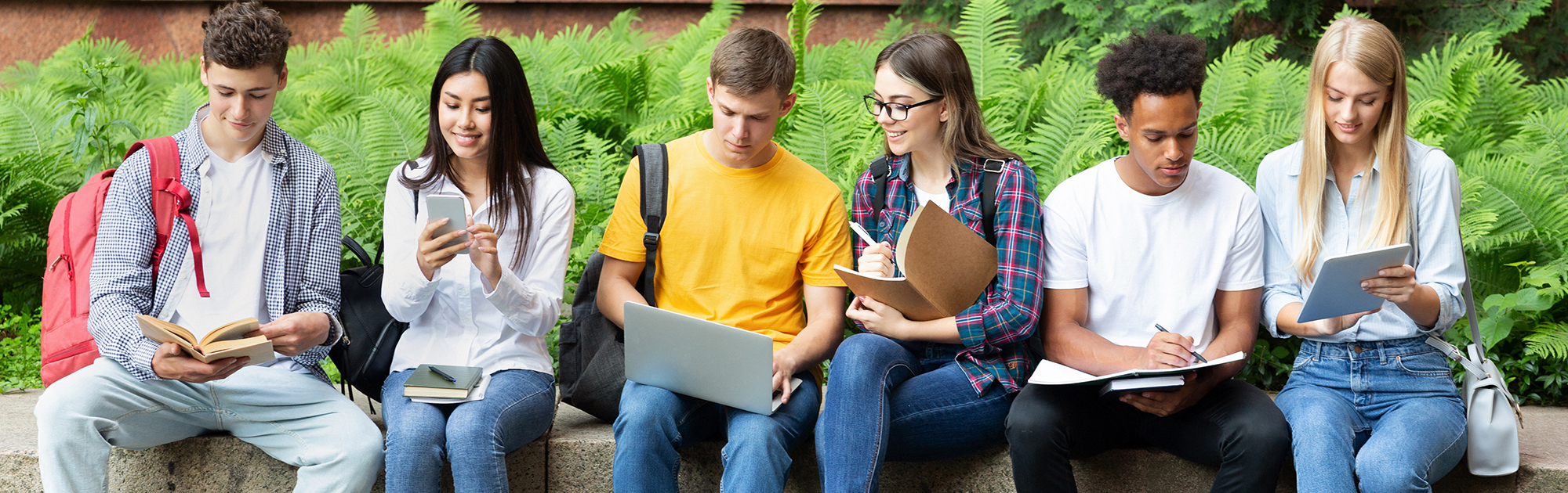 group of college students sitting and smiling using electronic devices